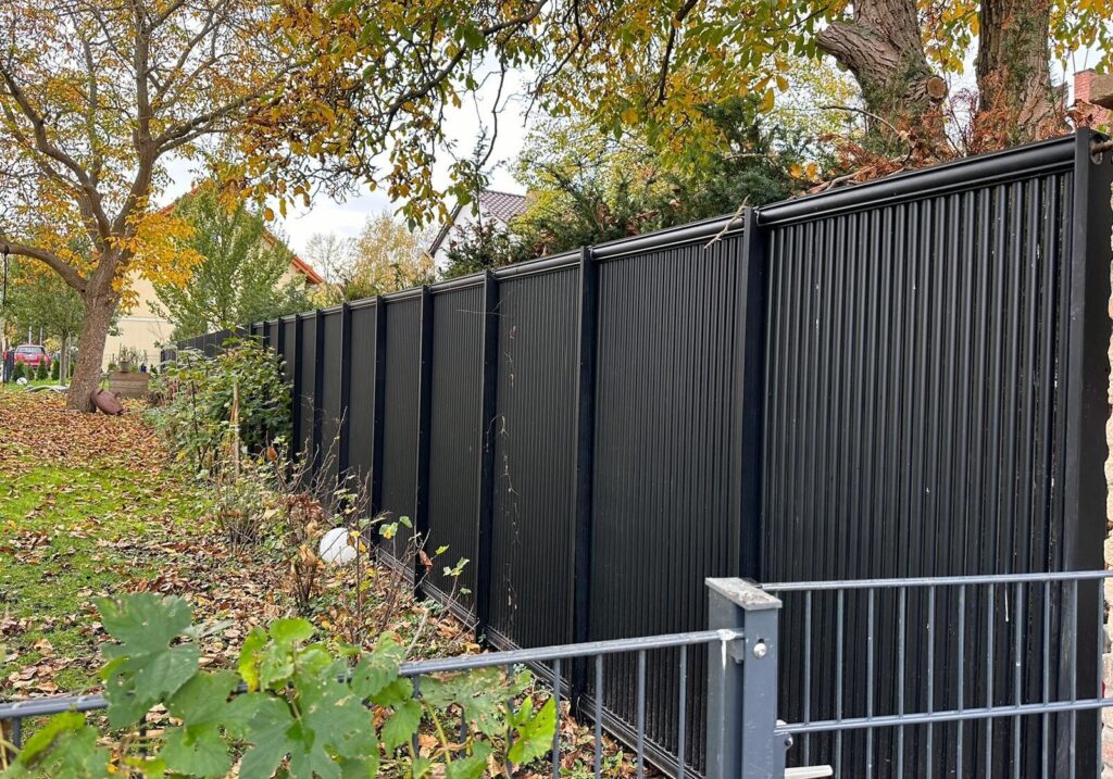 AluKol® Zaun entlang eines Grundstücks mit Baum- und Heckenbestand.