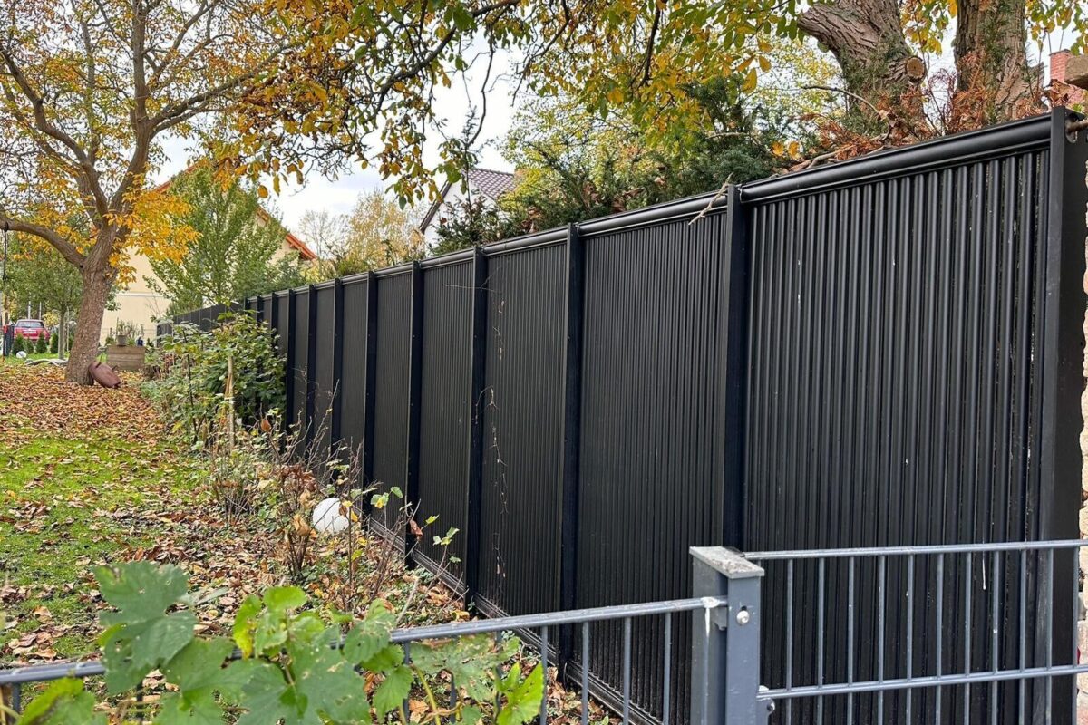 AluKol® Zaun entlang eines Grundstücks mit Baum- und Heckenbestand.